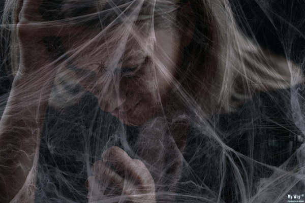 Eine niedergeschlagene, angespannte Frau befindet sich im Dunklen hinter einem Netz aus spinnenwebartigem Gewebe