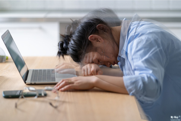 Eine Frau liegt erschöpft vornüber gebeugt auf Schreibtisch und Tastatur des Laptops