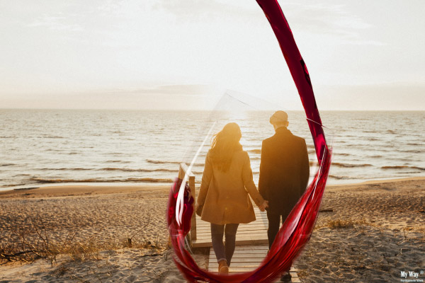 Ein Paar geht Hand in Hand am Strand auf einen Sonnenuntergang zu. Im Vordergrund wird ein Weinglas schwungvoll eingeschenkt und umrahmt die vertraute Szene.