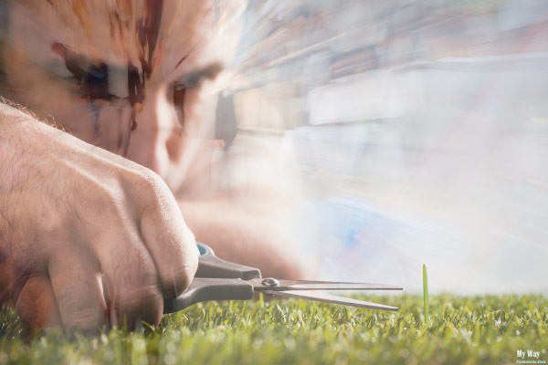 Mann schneidet mit einer Schere einzeln Grashalme, wirkt konzentriert und perfektionistisch. Der Bildhintergrund ist unruhig und hektisch