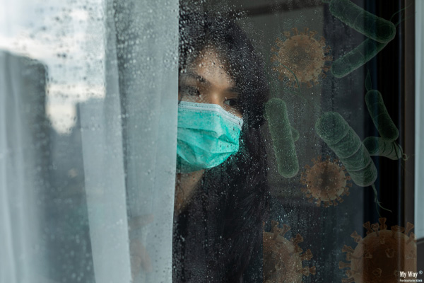Frau mit Mundschutz blickt durch ein regennasses Fenster, während symbolisch dargestellte Viren und Bakterien ihre Angst vor Krankheiten und ihre Hypochondrie verdeutlichen