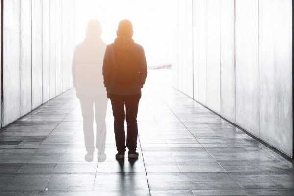 Eine Person geht durch einen hell erleuchteten Gang, neben ihr erscheint eine halbtransparente zweite Silhouette der selben Person als Symbol für das gleichzeitige Bestehen mehrerer Erkrankungen, das man Komorbidität nennt