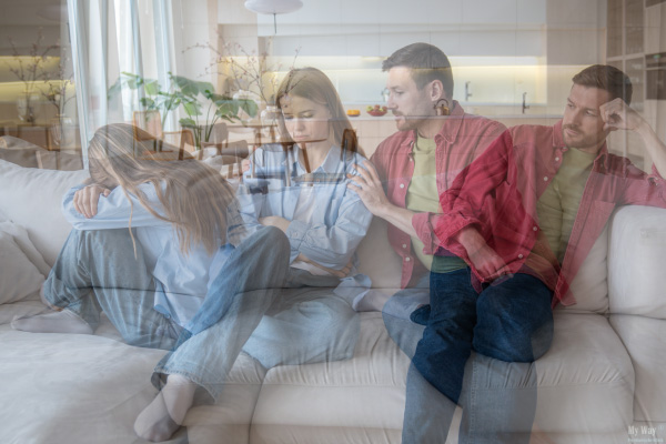 Junge Frau sitzt zusammengesunken auf und emotional belastet einem Sofa, während ein Mann neben ihr gestikuliert, symbolisch für psychische Gewalt in einer Beziehung