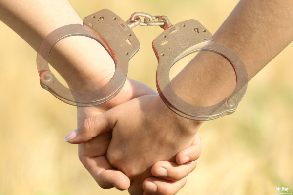 Zwei Menschen halten sich an den Händen, während beide Handgelenke mit halbtransparenten Handschellen verbunden sind