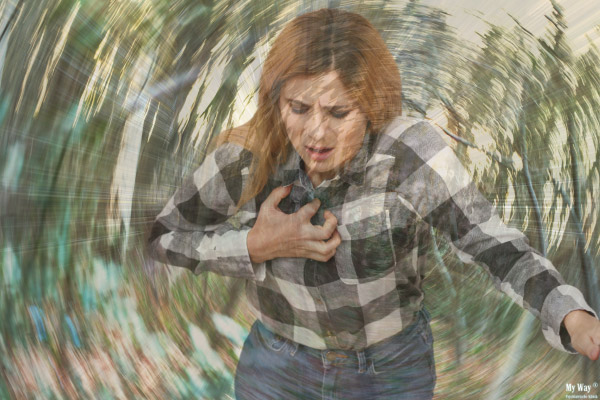 Frau hält sich mit verzerrtem Gesicht die Brust, während sich die Umgebung verschwommen und drehend darstellt, als Symbol für eine starke Panikattacke