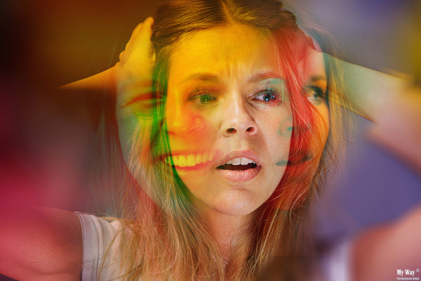 Eine weibliche Person zeigt einen angespannten Gesichtsausdruck, während ihr Gesicht mehrere, verzerrte und bunte Überlagerungen aufweist, die einen Zustand innerer Zerrissenheit oder Verwirrung darstellen