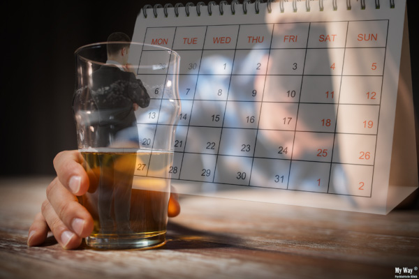Ein Glas Bier, in dem ein Mann steht, der auf einen riesigen Kalender blickt. Symbolbild für Quartalstrinken und episodischen Alkoholkonsum