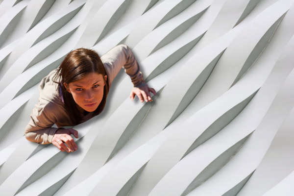 Frau klettert an einer strukturierten, wellenförmigen weißen Wand, Blick nach oben gerichtet, als Symbol für den in wellen auftretenden Kampf gegen Rückfälle und den Weg zurück in die Stabilität